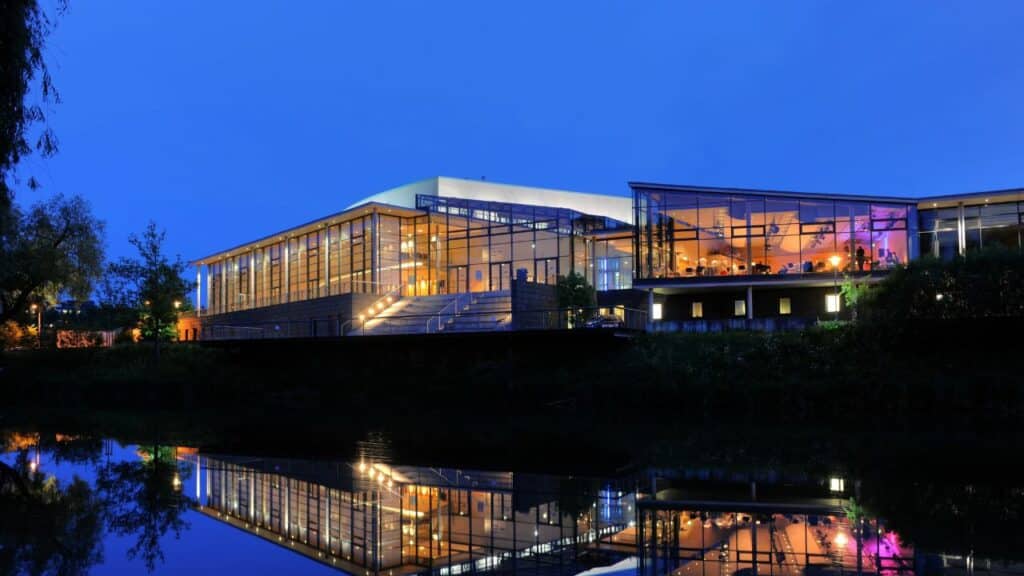 Die Tuttlinger Hallen von außen am Abend. Im Vordergrund spiegelt sich die Stadthalle in einem See.