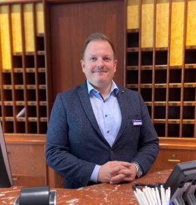 Ein Bild des Direktors des BestWestern Parkhotels, Herrn Matthias Schenk, der lächelnd an der Hotel Rezeption steht.