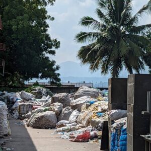 Plastik-Müllberg auf den Philippinen neben einer Lagerhalle. Zwischen Palmen und blauem Himmel lagert der Plastikmüll, der von Click A Tree aus dem Meer gesammelt wurde.