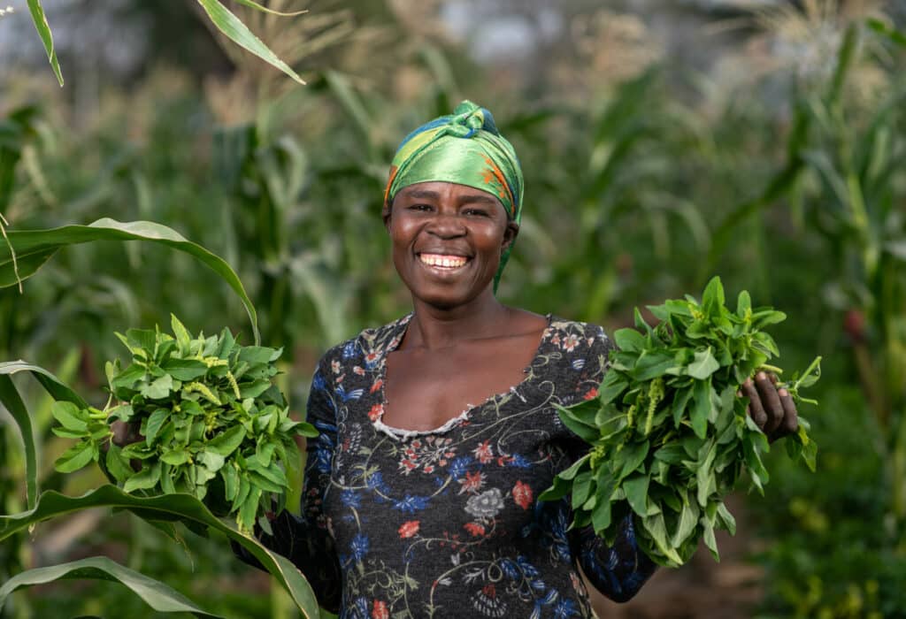 Eine Frau in Ghana lächelt herzlich und hält in beiden Händen Baumsetzling
