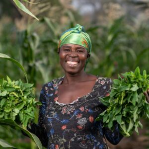 Eine Frau in Ghana lächelt herzlich und hält in beiden Händen Baumsetzling